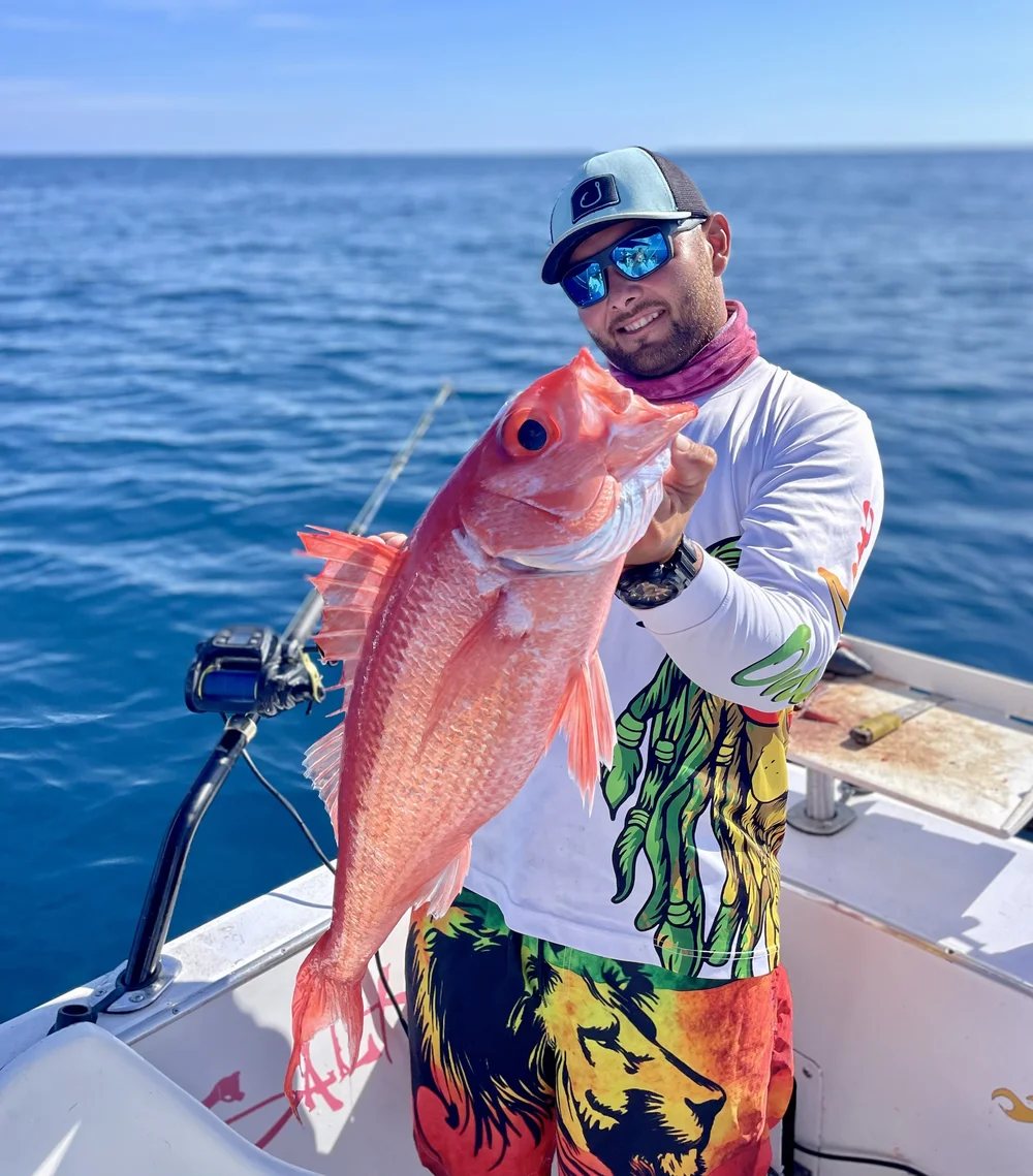 An angler on a fishing boat holding up a big red snapper, with blue open water behind