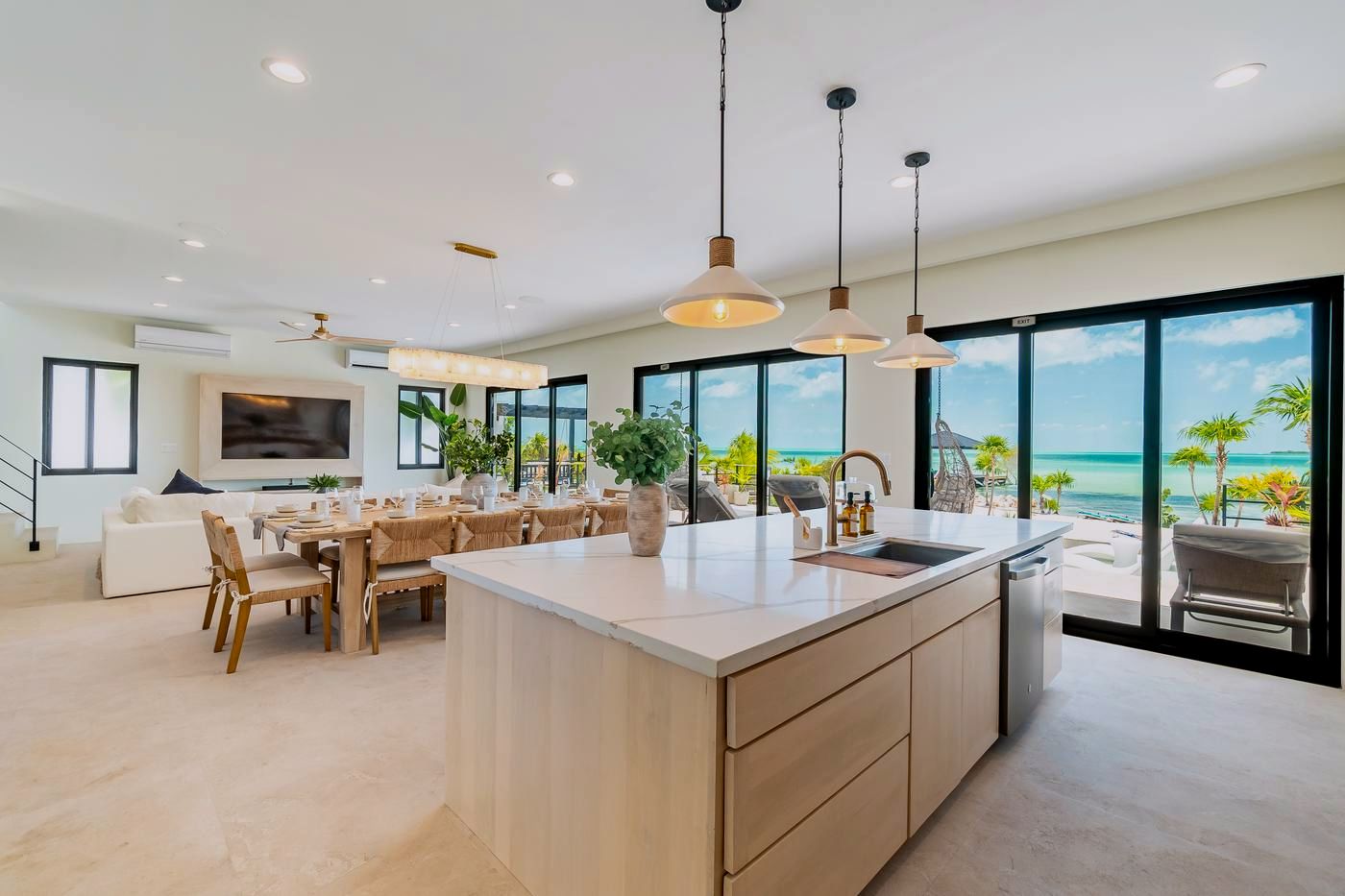 The great room: kitchen island, dining table and lounge behind floor-to-ceiling windows on the sea