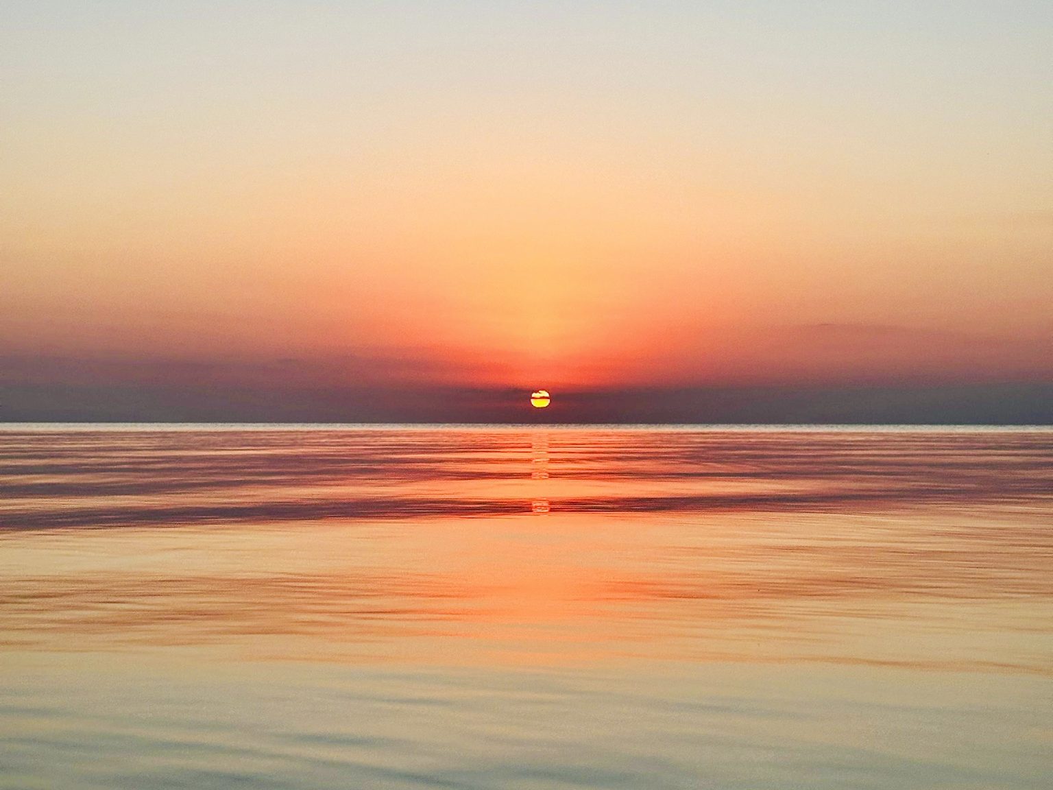 The sun setting over calm water off the west shore of Ambergris Caye, seen from Secret Beach