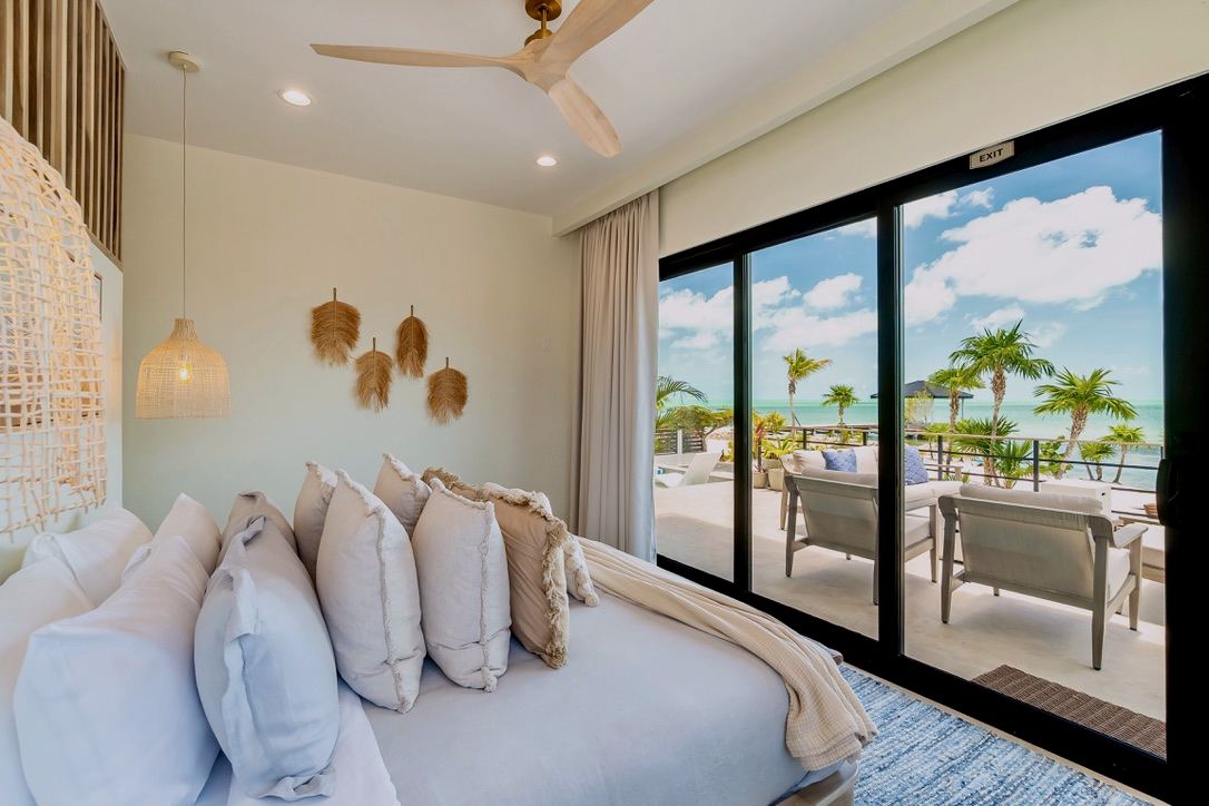 The Primary Suite: a king bed facing glass doors to a private deck over the water