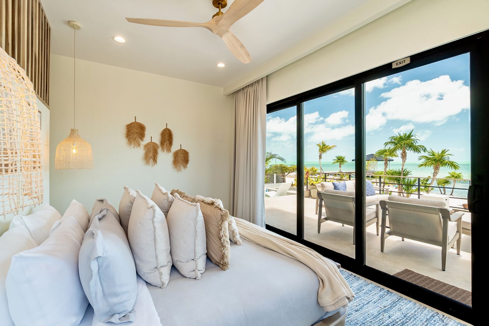 The Primary Suite: king bed behind a wall of glass that opens to a private deck over the water